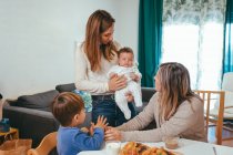 Allegro donna omosessuale con piccolo bambino in piedi vicino al tavolo con la fidanzata e il figlio durante i pasti — Foto stock