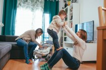 Smiling young lesbian couple playing with adorable little kids while spending free time together in modern living room — Stock Photo