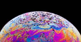 Vista panorámica del fondo texturizado de la burbuja de primer plano que representa el planeta colorido con líneas onduladas en la superficie en forma redonda sobre fondo negro - foto de stock