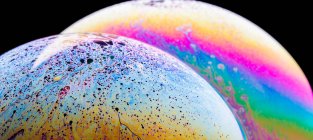 Panoramic view of closeup bubble textured backdrop representing colorful planets with wavy lines on round shaped surface on black background — Stock Photo