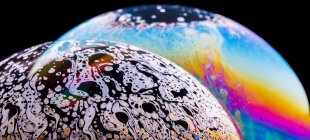 Vue panoramique de gros plan bulle texturé toile de fond représentant des planètes colorées avec des lignes ondulées sur la surface de forme ronde sur fond noir — Photo de stock