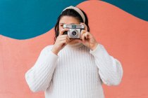 Анонімні зосереджені жінки в повсякденному одязі фотографують на цифровій камері біля яскравої стіни в денне світло — стокове фото