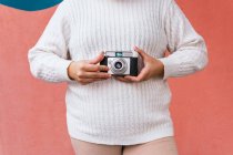Анонимная женщина в повседневной одежде фотографирует на цифровую камеру возле яркой стены при дневном свете — стоковое фото
