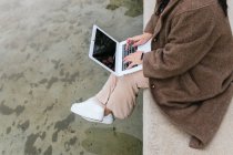 Von oben Seitenansicht der Ernte anonyme Plus-Size-Frau surft im Internet auf Netbook mit schwarzem Bildschirm über Teich in der Stadt — Stockfoto