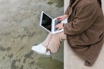 From above side view of crop anonymous plus size female surfing internet on netbook with black screen above pond in town — Stock Photo