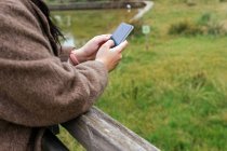 Ritaglio anonimo di giovane paffuto femmina in cappotto navigare internet sul cellulare in città — Foto stock