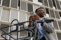 Низький кут змісту Афроамериканський менеджер чоловічої статі пише текстові повідомлення на мобільному телефоні біля велосипеда в місті. — стокове фото