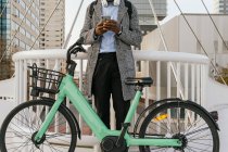 Low angle of anonymous content African American male manager in headset text messaging on cellphone near bicycle in town — Stock Photo