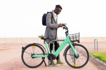 Side view of African American male office employee using app on cellphone while parking bike in city — Stock Photo