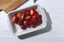 Top view yummy ripe strawberries without calyx heaped on white plate near cutting board on table — Stock Photo