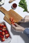 Top view crop unrecognizable chef in latex gloves cutting fresh delicious strawberries on wooden cutting board on table — Stock Photo