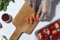 Top view crop unrecognizable chef in latex gloves cutting fresh delicious strawberries on wooden cutting board on table — Stock Photo