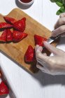 Top vista cultura chef irreconhecível em luvas de látex cortar morangos deliciosos frescos na tábua de corte de madeira na mesa — Fotografia de Stock