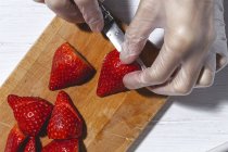 Ernte von oben bis zur Unkenntlichkeit Koch in Latex-Handschuhen schneiden frische köstliche Erdbeeren auf Holz Schneidebrett auf dem Tisch — Stockfoto