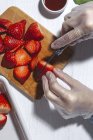 Неузнаваемый шеф-повар в латексных перчатках режет свежую вкусную клубнику на деревянной доске на столе — стоковое фото