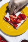 Top view crop anonymous chef in glove arranging cut strawberries on bread toast with spread cream cheese — Stock Photo
