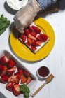 Chef anonyme en gant organisant des fraises coupées sur pain grillé au fromage à la crème tartiné — Photo de stock