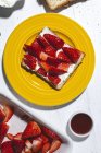 Композиция из сладких тостов со сливочным сыром и спелой клубникой на желтой тарелке на столе — стоковое фото