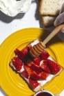 Анонимная опытная шеф-повар в перчатках наливает сладкий мед на вкусный тост со сливочным сыром и режет клубнику во время приготовления пищи на светлой кухне — стоковое фото