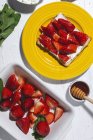 Composición aérea de tostadas dulces con queso crema y fresas maduras servidas en plato amarillo sobre la mesa - foto de stock