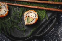 Composition vue du dessus de délicieux sushi frais divers et baguettes de bambou servis sur plateau noir sur tissu à carreaux — Photo de stock