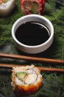 Savoureux sushi frais assorti servi sur des brindilles de plantes vertes sur une assiette noire avec sauce soja sur une table en marbre près de baguettes — Photo de stock