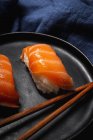 Composition vue du dessus de délicieux sushis frais et baguettes de bambou servis sur plateau noir sur tissu à carreaux — Photo de stock