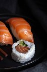 Composizione vista dall'alto di deliziosi sushi freschi e bacchette di bambù servite su piatto nero su un panno a scacchi — Foto stock
