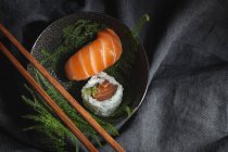 Вкусные свежие суши подаются на зеленых ветках растений на черной тарелке с соевым соусом на мраморном столе рядом с палочками для еды — стоковое фото