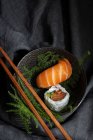 Sabroso sushi fresco servido en ramitas de plantas verdes en plato negro con salsa de soja en mesa de mármol cerca de palillos - foto de stock