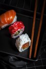Top vista composição de deliciosos sushi fresco e vários pauzinhos de bambu servido em prato preto em pano xadrez — Fotografia de Stock