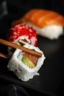 Zusammensetzung von köstlichen frischen verschiedenen Sushi und Bambusstäbchen, serviert auf schwarzer Platte auf kariertem Tuch — Stockfoto