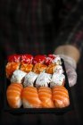 Неузнаваемый шеф-повар в перчатках показывает блюдо с набором вкусных суши в темной комнате — стоковое фото