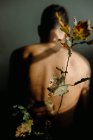 Anonymes Männchen ohne Hemd sitzt in dunklem Raum neben zartem dünnem Pflanzenzweig mit welkenden Blättern — Stockfoto