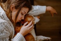 Top view of crop young female in warm sweater hugging adorable purebred dog while sleeping together on sofa at home — Stock Photo