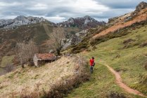 Vue latérale Voyageur sans visage debout sur un sentier rural sur une pente herbeuse dans un terrain montagneux spacieux par temps couvert dans les Asturies Espagne — Photo de stock