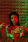 Ernte anonyme Menschen heben die Hände mit Essstäbchen in der Nähe erstaunt asiatische Frau mit Schale mit Nudeln — Stockfoto