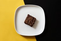 Piece of fresh brownie on black and yellow background — Stock Photo