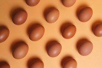 Fundo sem costura de ovos marrons colocados em fileiras na mesa laranja no estúdio — Fotografia de Stock