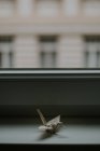 Origami en papier fait main représentant des grues similaires contre la fenêtre et la façade de la maison au crépuscule sur fond flou — Photo de stock