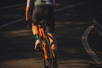 Back view of young sportsman in activewear and helmet riding bicycle on asphalt road amidst lush green trees on sunny day — Stock Photo
