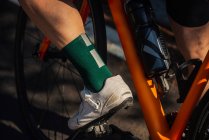 Врожай невідомий велосипедист у шортах та кросівках, що їздять сучасним велосипедом на сонячній літній вулиці — стокове фото