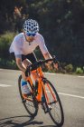 Corpo inteiro de jovem desportista em activewear e capacete andar de bicicleta na estrada de asfalto no dia ensolarado — Fotografia de Stock