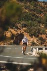 Полное тело молодого спортсмена в спортивной одежде и шлеме на велосипеде по асфальтированной дороге в солнечный день — стоковое фото