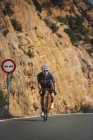 Повне тіло юного спортсмена в активному одязі і шоломі їде на велосипеді по асфальтовій дорозі в сонячний день — стокове фото