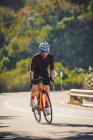 Corps complet de jeune sportif en vêtements de sport et casque vélo d'équitation sur route asphaltée par une journée ensoleillée — Photo de stock