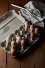 Сверху контейнера с яйцами, размещенными возле венчика на салфетке на кухне — стоковое фото