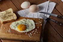 From above of appetizing fried eggs served with fresh bread on wooden chopping board — Stock Photo
