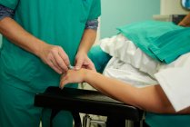 Colheita assistentes médicos irreconhecíveis inserindo cateter intravenoso na mão em paciente anônimo deitado no sofá na sala de cirurgia — Fotografia de Stock