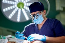 Неузнаваемый врач-мужчина в медицинской форме и увеличительных очках, выполняющий ринопластику для анонимного пациента, лежащего на диване в операционной — стоковое фото